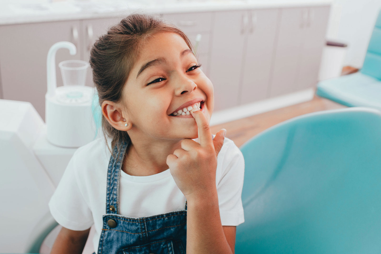 little patient showing her perfect toothy smile while sitting dentists chair