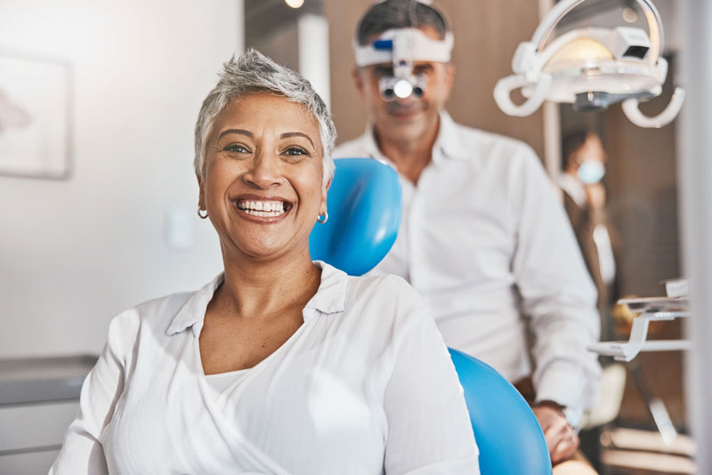 Smiling dental patient sitting in a treatment chair with a dentist in the background, creating a positive and welcoming dental office experience.